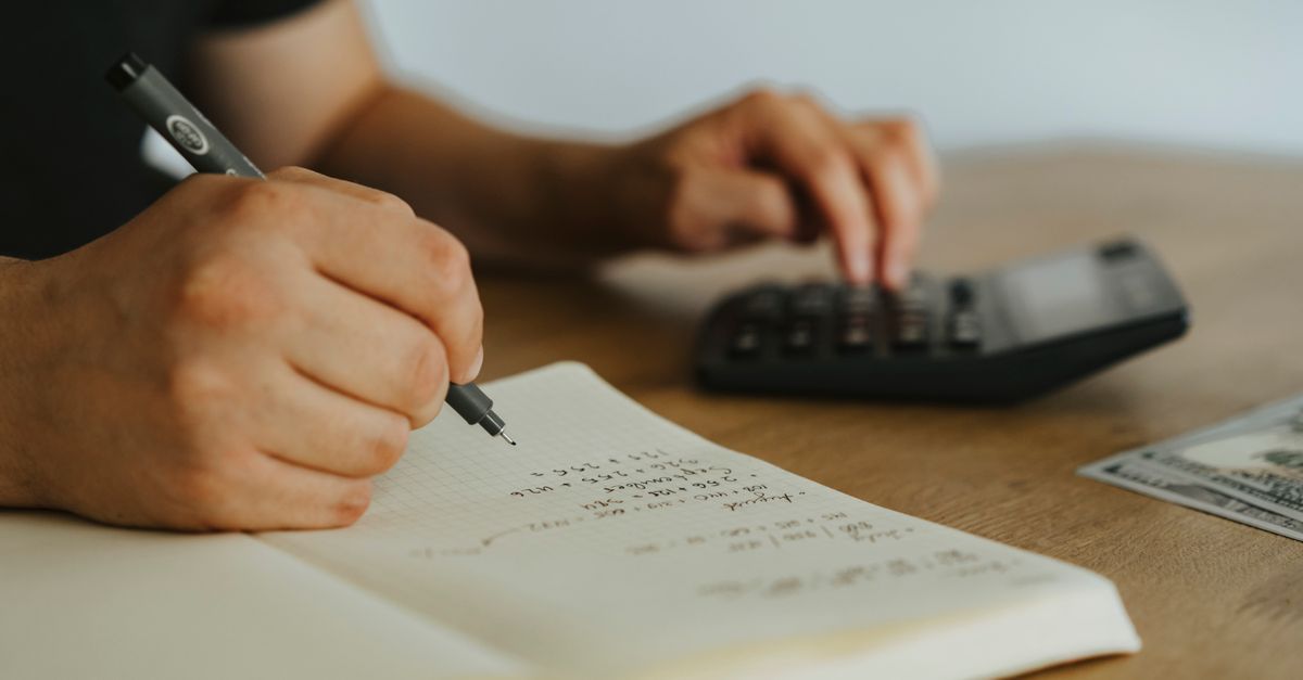 Someone working through figures in a notebook beside a calculator