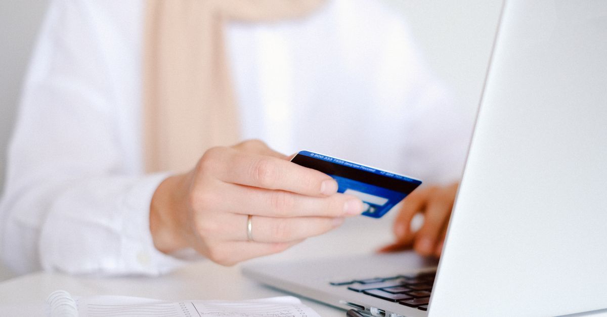 Someone holding a credit card while using a laptop