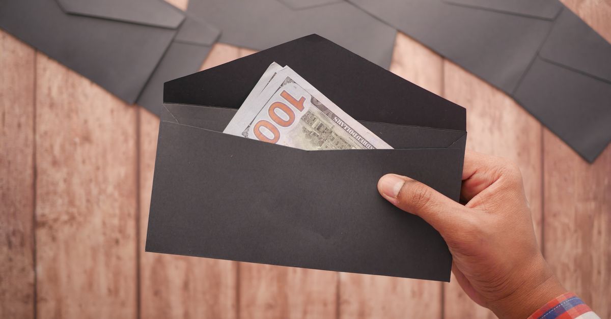 A hand placing hundred dollar bills into an envelope